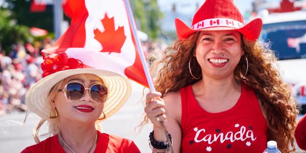 Two women smiling at the Canada Day parade with flags in hand