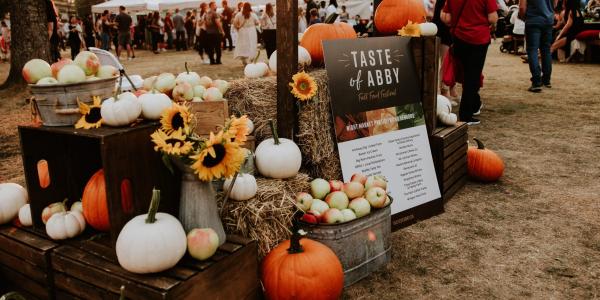 A rustic autumnal display at the ‘Taste of Abby’ festival featuring pumpkins, apples, hay bales, and a festive sign.