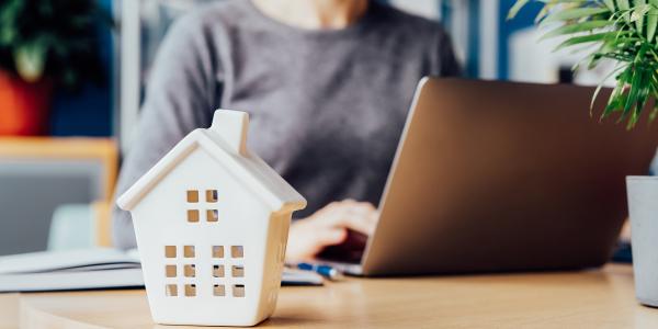 Small house on desk with a woman at a laptop